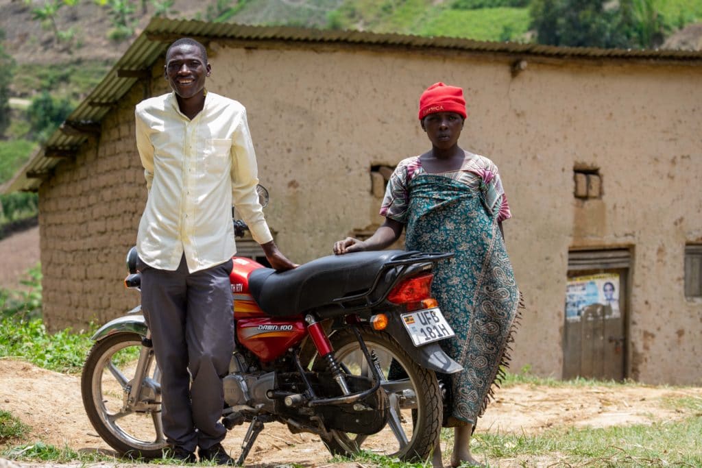 Kadogo smiles while standing with his motorbike and Jovia.